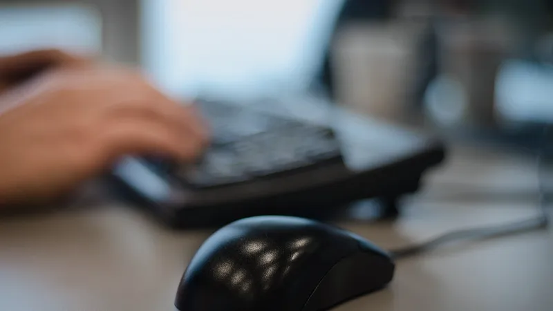 Hands typing at a keyboard beside a mouse on an office desk